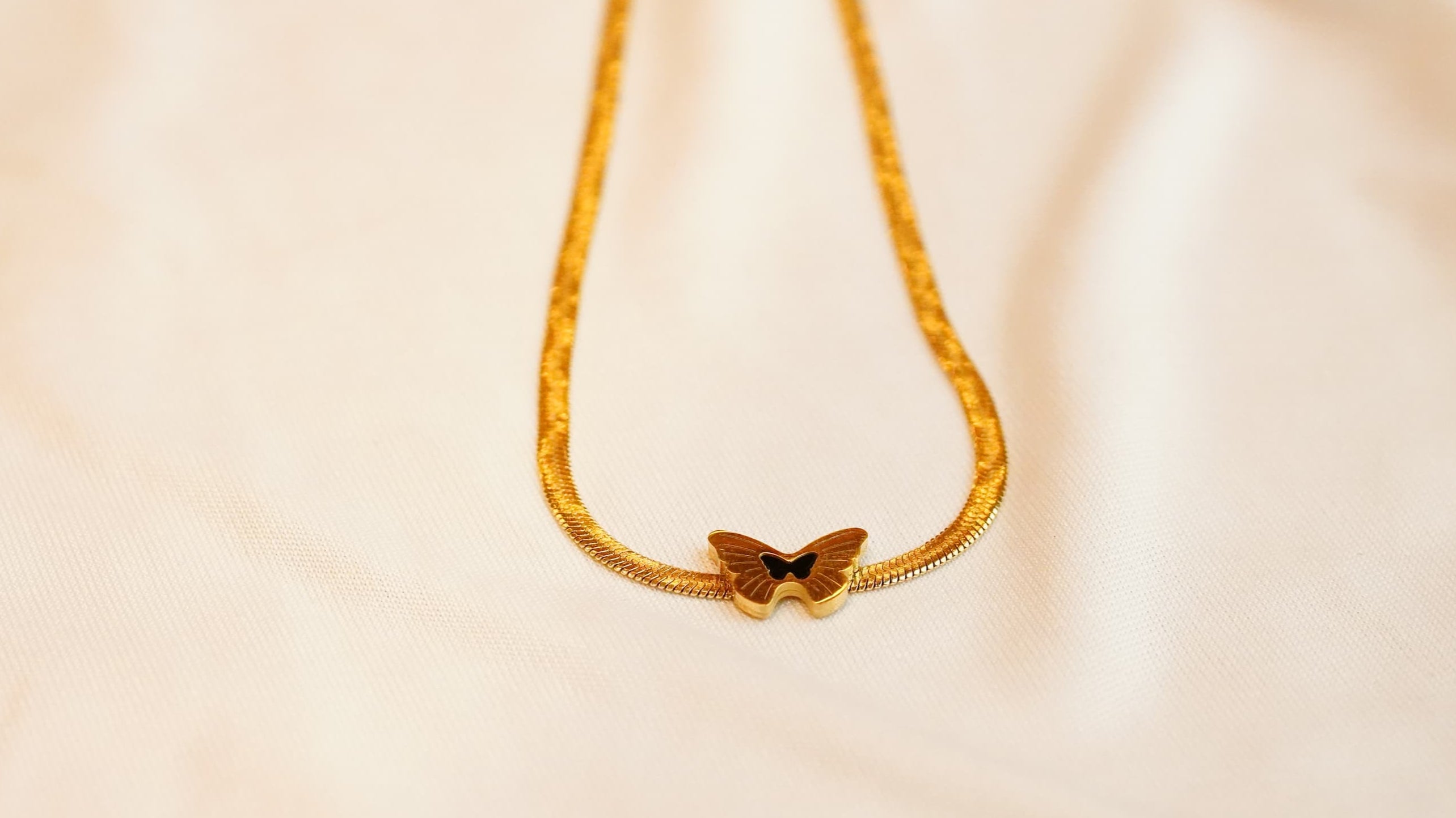 Gold ss necklace with a butterfly pendant on a beige background