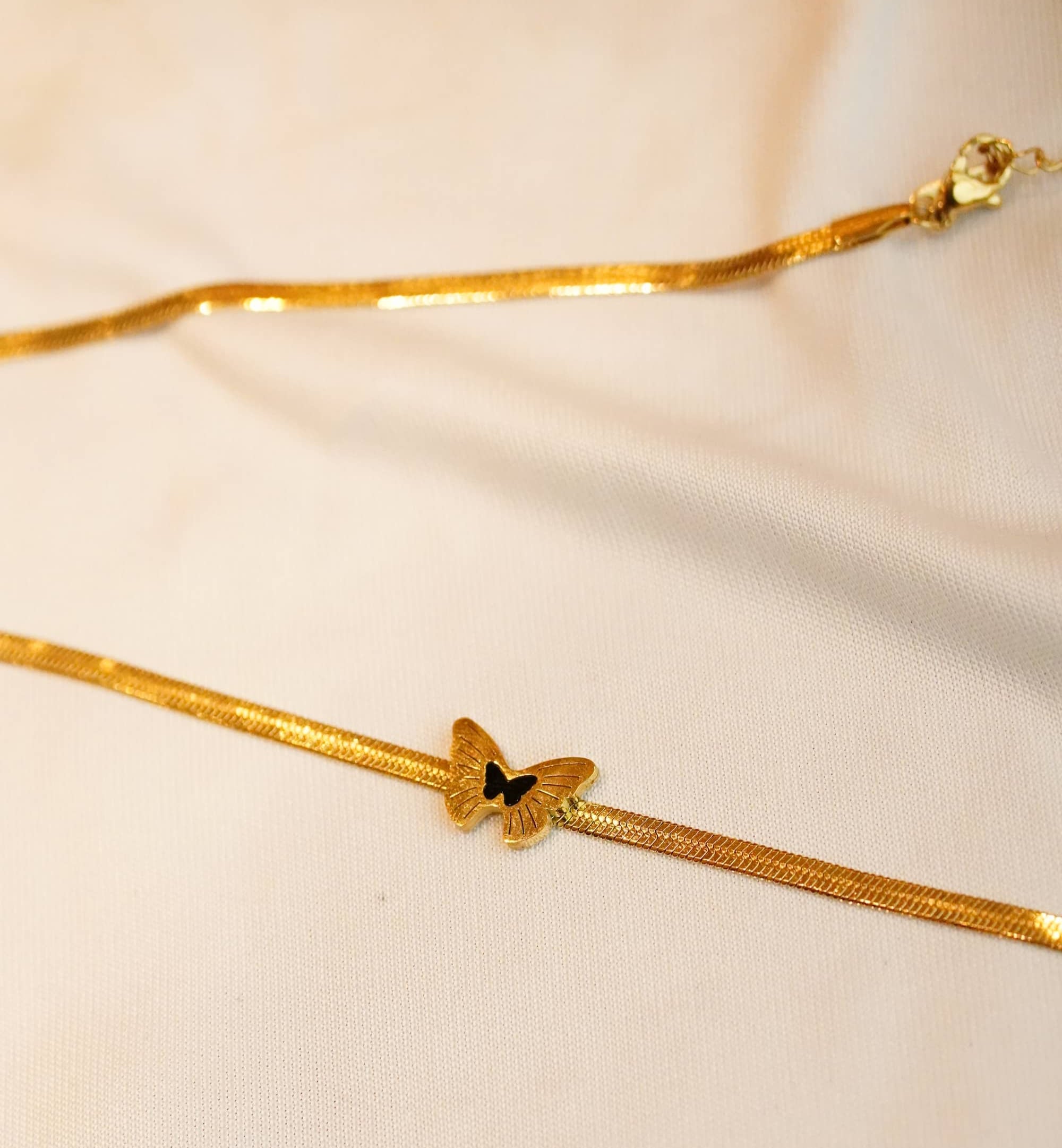 Gold ss bracelet with a butterfly charm on a beige fabric background