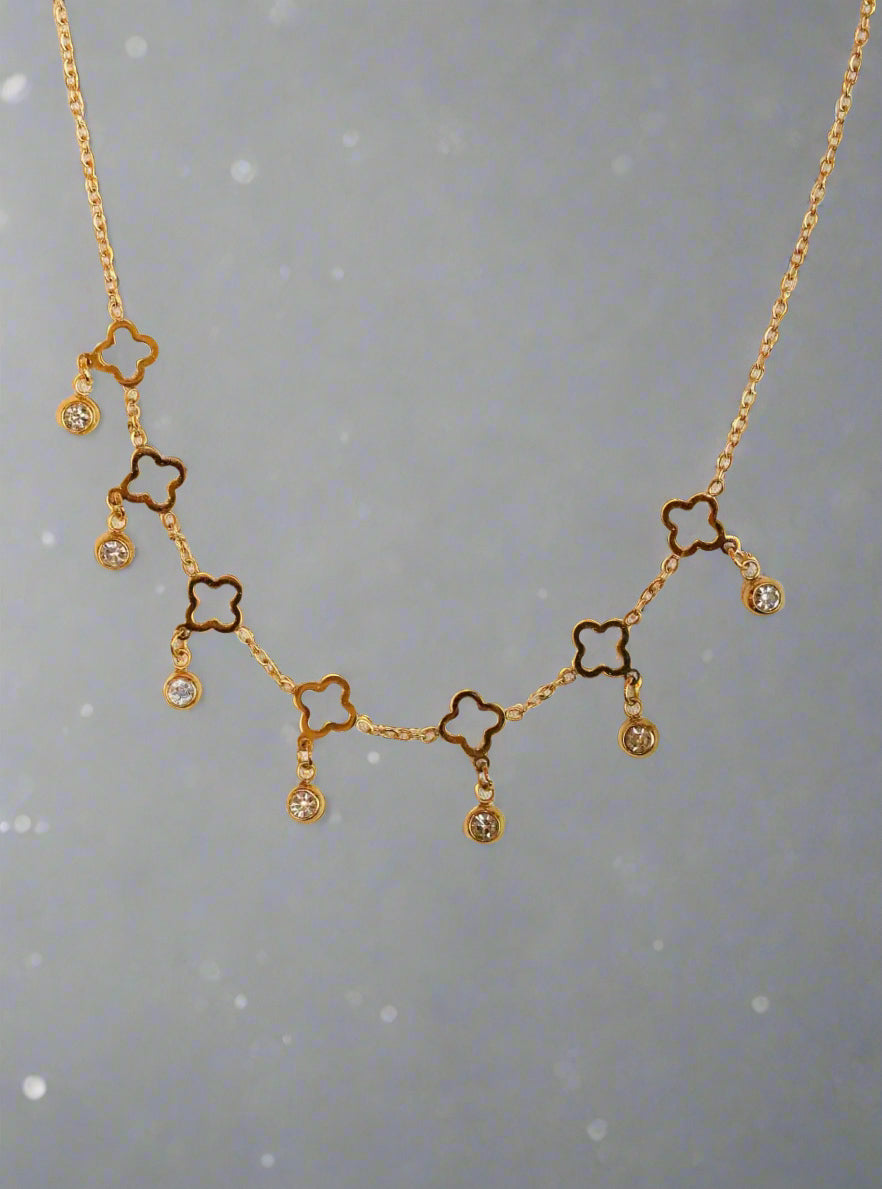 Gold ss necklace with clover-shaped pendants on a soft pink background