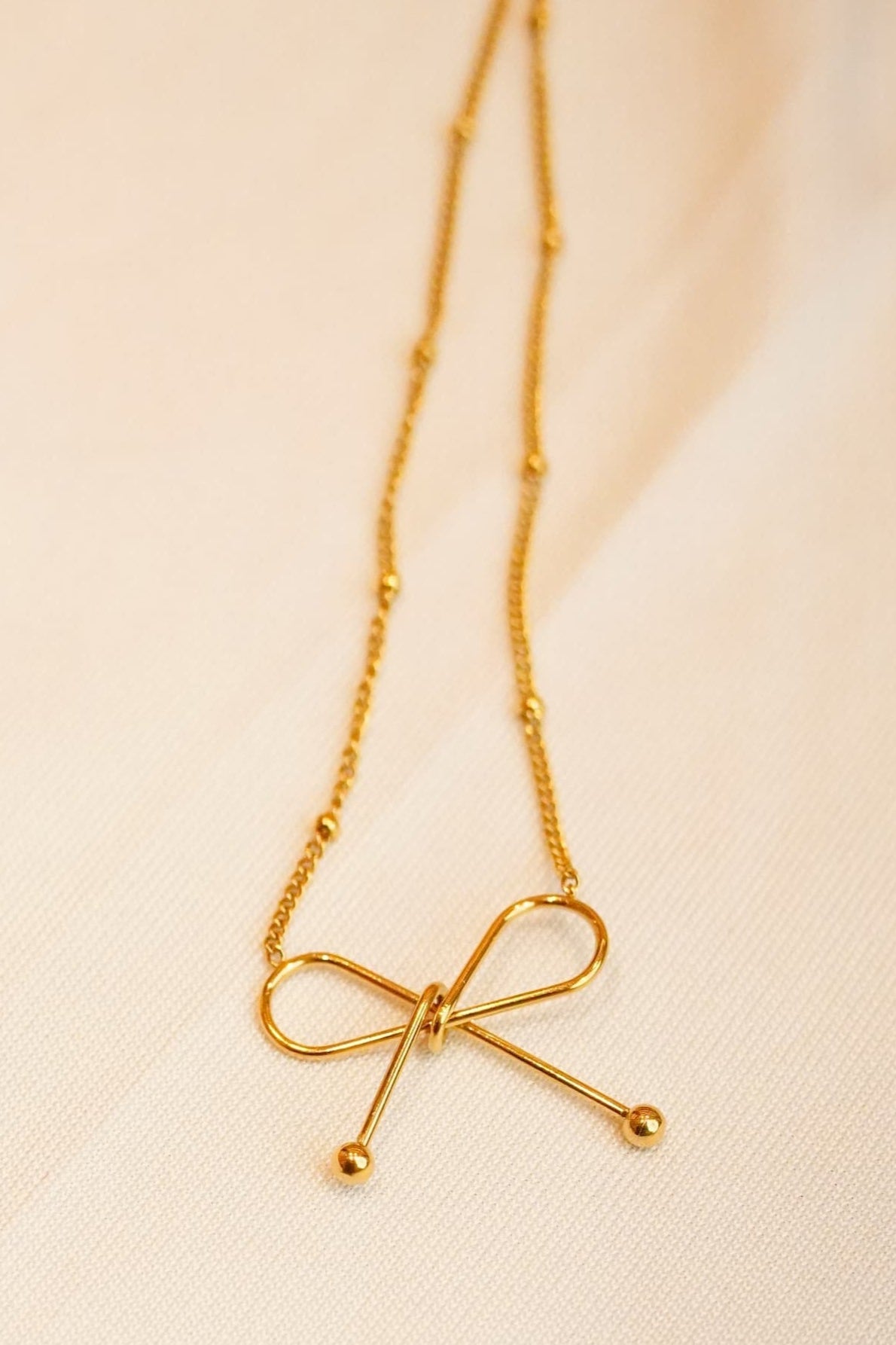 Gold ss necklace with a bow-shaped pendant on a soft beige background