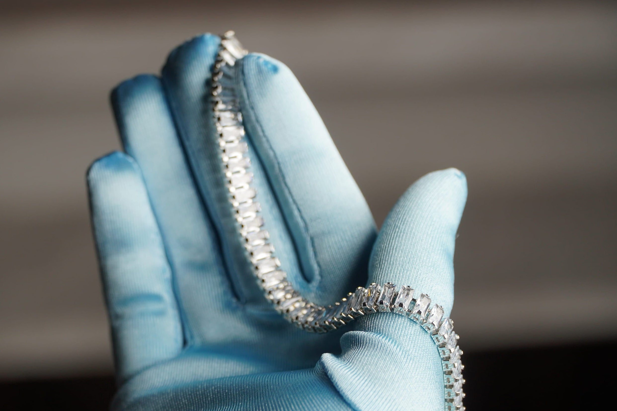 Silver bracelet held by a hand wearing a light blue glove against a blurred background