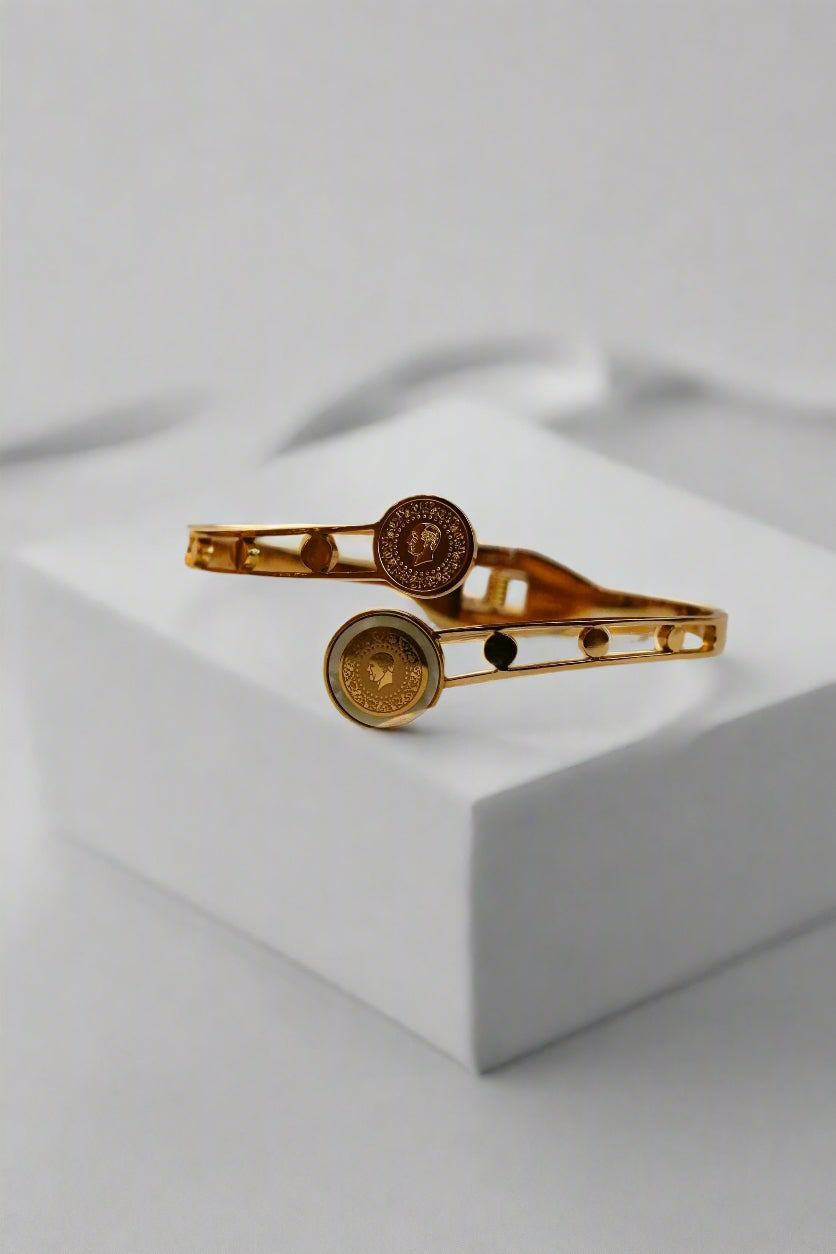 Gold ss bracelet with circular designs on a textured beige surface