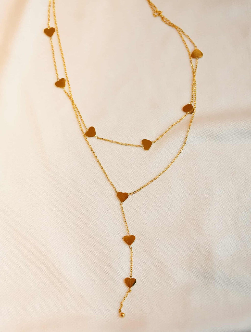 Gold ss necklace with heart-shaped pendants on a light background