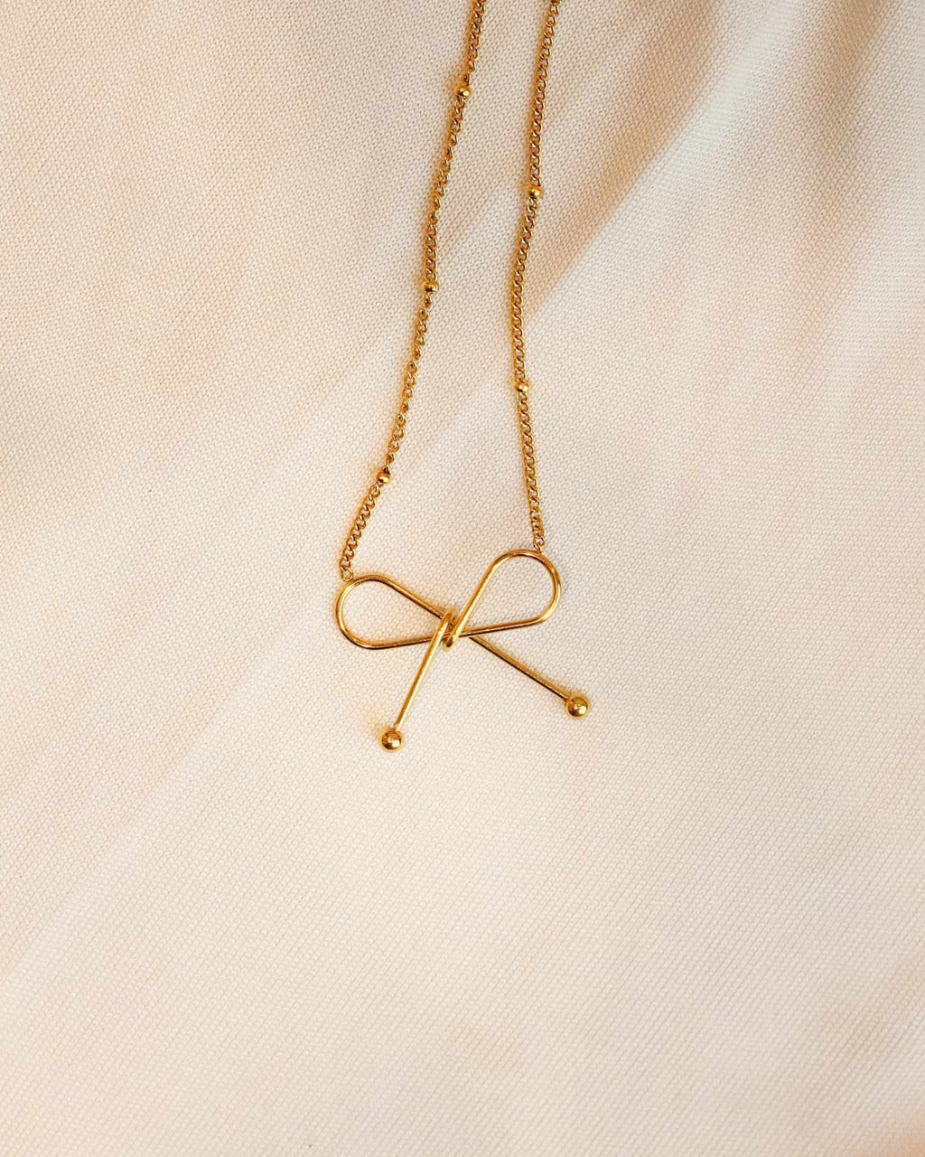 Gold ss necklace with a bow pendant on a soft beige background